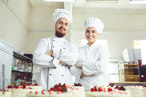 Pastry chefs in white uniform are smiling at bakery.