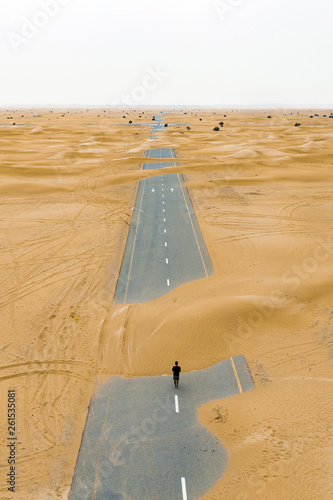 Photography View from above, stunning aerial view of an unidentified person walking on a deserted road covered by sand dunes in the middle of the Dubai desert