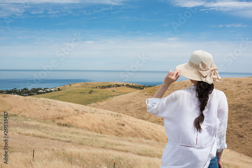 Woman in sunhat looking at rolling hills and ocean Australian landscape