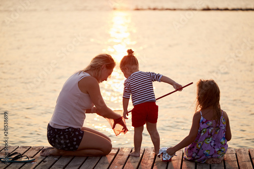 Happy kids playing with mother on the beach at the sunrise time with fishing net. Family and friendships concept. Summer time