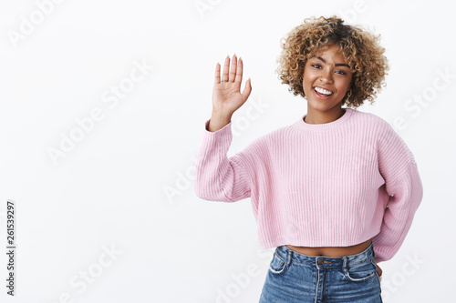 Hey give me high five. Friendly, joyful charismatic girlfriend with blond afro haircut in winter stylish sweater raising palm greet friend or wave smiling joyfully and cute at camera over white wall photo