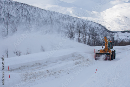 Snow plow truck clearing icy road after winter snowstorm blizzard for vehicle access Snow blower clears snow-covered streets producing a plume of snow. Winter landscape in Norway or Sweden Scandinavia