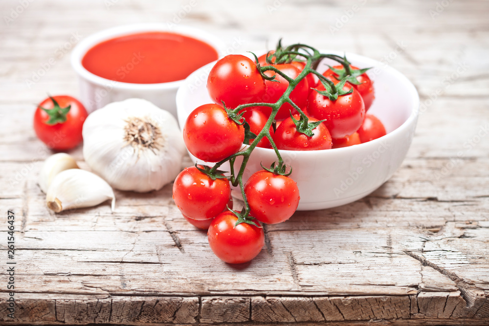 Fresh tomatoes in white bowl, sauce and raw garlic on rustic wooden table. Fresh tomatoes in white bowl, sauce and raw garlic on rustic wooden table.