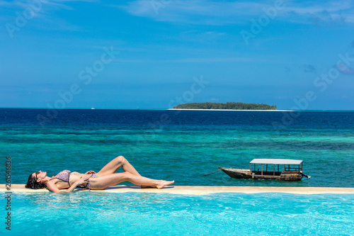 one caucasian woman enjoying vacations sunbathing on a infinity swimming pool by the seaside looking at the idian ocean Muyuni in Unguja aka Zanzibar Island Tanzania East Africa