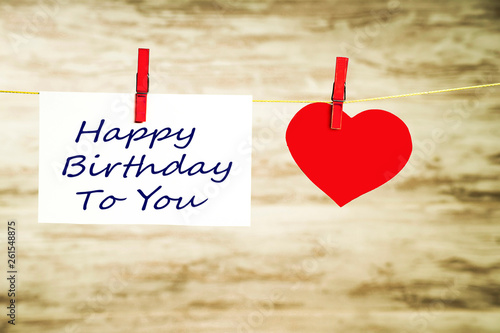 A white card and a red heart hanging on a string, fastened with red buckles with the words Happy Birthday
