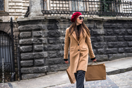 Attractive cute girl in with the shopping bags. Young beautiful woman with long brown hair in sunglasses on a walk on a cloudy day. Fashionable sexy girl. Street fashion look. Cute student. Shopping.