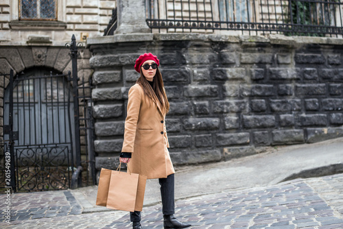 Attractive cute girl in with the shopping bags. Young beautiful woman with long brown hair in sunglasses on a walk on a cloudy day. Fashionable sexy girl. Street fashion look. Cute student. Shopping.