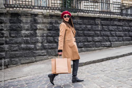 Attractive cute girl in with the shopping bags. Young beautiful woman with long brown hair in sunglasses on a walk on a cloudy day. Fashionable sexy girl. Street fashion look. Cute student. Shopping.