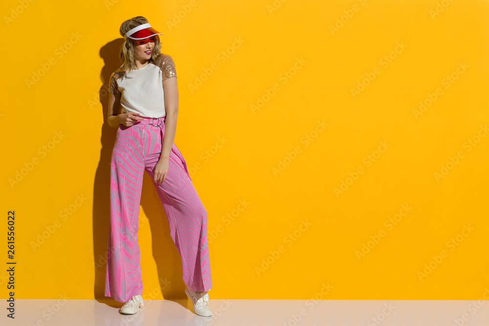 Smiling Fashion Model In Striped Wide Legs Trousers And Transparent Sun Visor Is Standing In The Sunlight