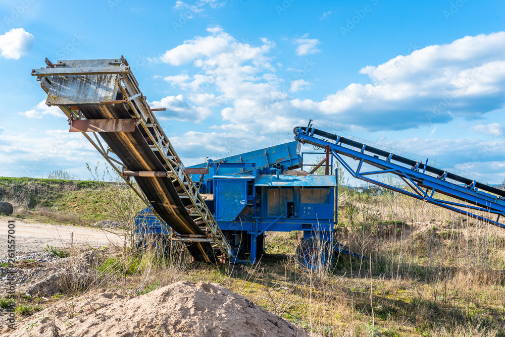 Old, mobile screen for gravel and sand in blue color standing on the field, in the background blue sky with clouds. Old, mobile screen for gravel and sand in blue color standing on the field, in the background blue sky with clouds.