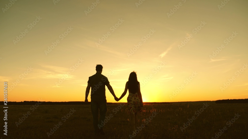 Young couple in love walking across the field holding hands. girl and man go to the sunset. happy family walks in the park in summer in the rays of sun. happy family concept