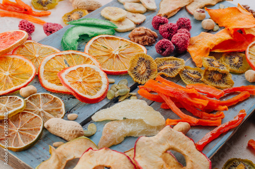 Mixed dried fruit and vegetable chips, candied pumpkin slices, nuts and seeds on blue wooden board photo