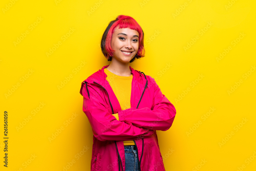 Young woman with pink hair over yellow wall keeping the arms crossed in frontal position Young woman with pink hair over yellow wall keeping the arms crossed in frontal position