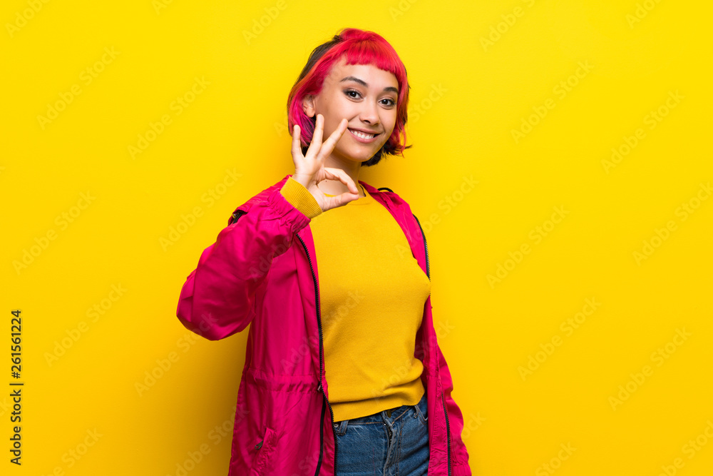 Young woman with pink hair over yellow wall showing ok sign with fingers Young woman with pink hair over yellow wall showing ok sign with fingers