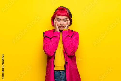 Young woman with pink hair over yellow wall with headache © luismolinero
