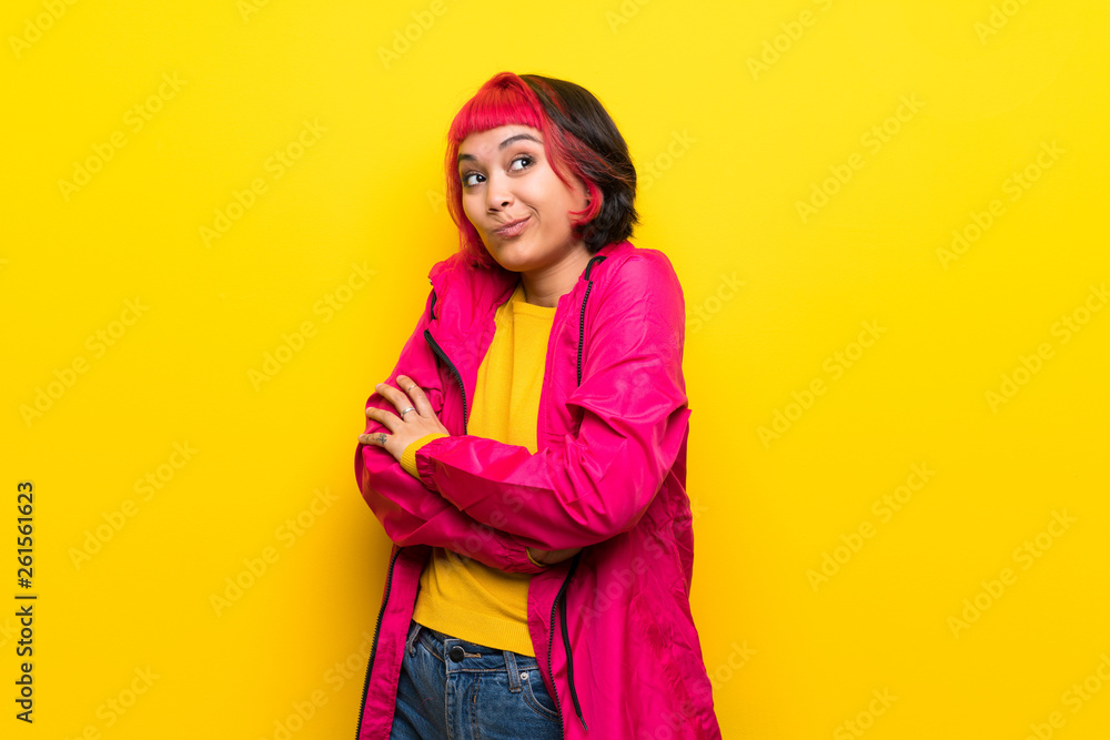 Young woman with pink hair over yellow wall making doubts gesture while lifting the shoulders Young woman with pink hair over yellow wall making doubts gesture while lifting the shoulders