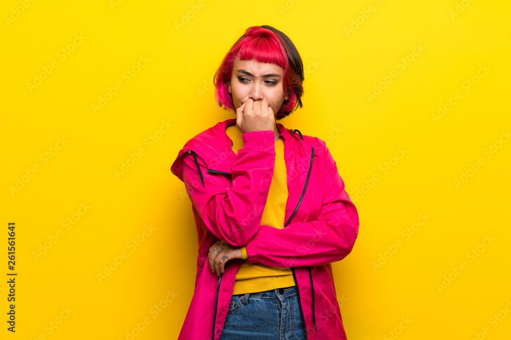 Fototapeta premium Young woman with pink hair over yellow wall having doubts