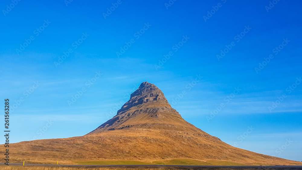 A close up on a stunning view on famous Iceland's mountain, Kirkjufell. Tall, hat-like mountain. Steep slopes of the hill. Beautiful and clear day, popular destination for a holiday.