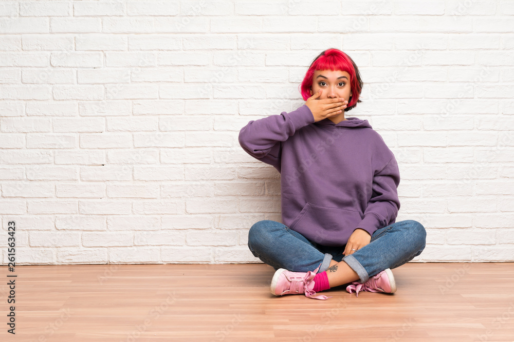 Young woman with pink hair sitting on the floor covering mouth with hands Young woman with pink hair sitting on the floor covering mouth with hands