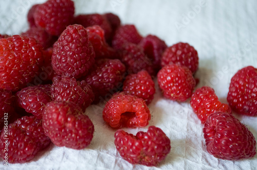 Big ripe raspberries are laying on the table covered with white tablecloth