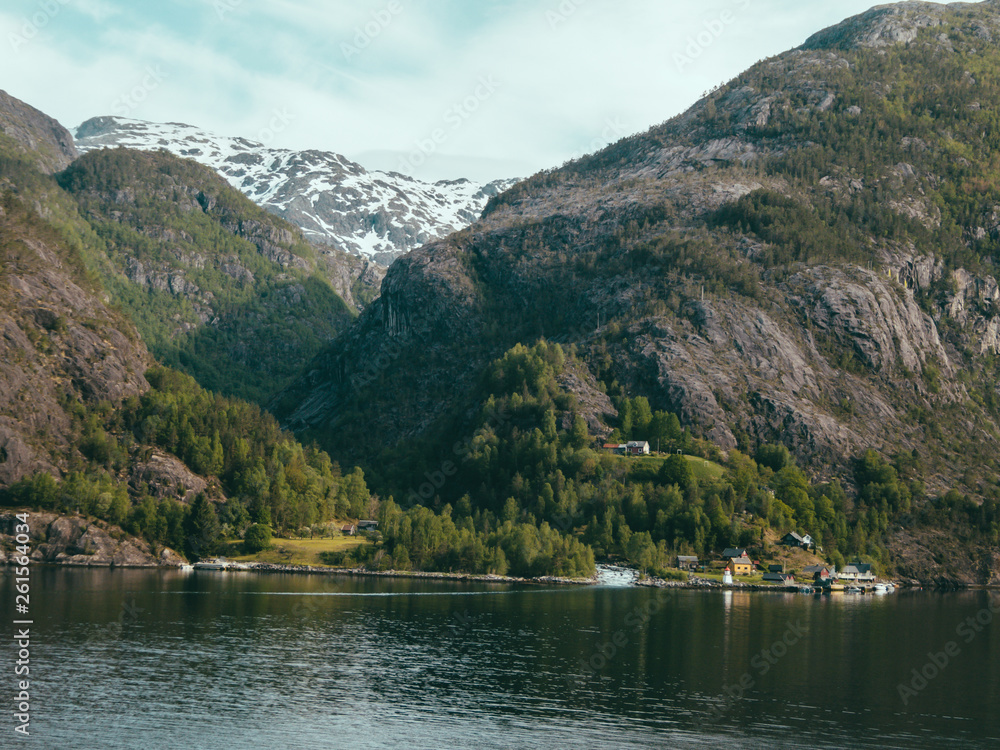 Åkrafjorden is a fjord in Hordaland county, Norway. Seen from the water level. Slopes are overgrown with green trees and bushes, in the back higher mountains are covered with snow.