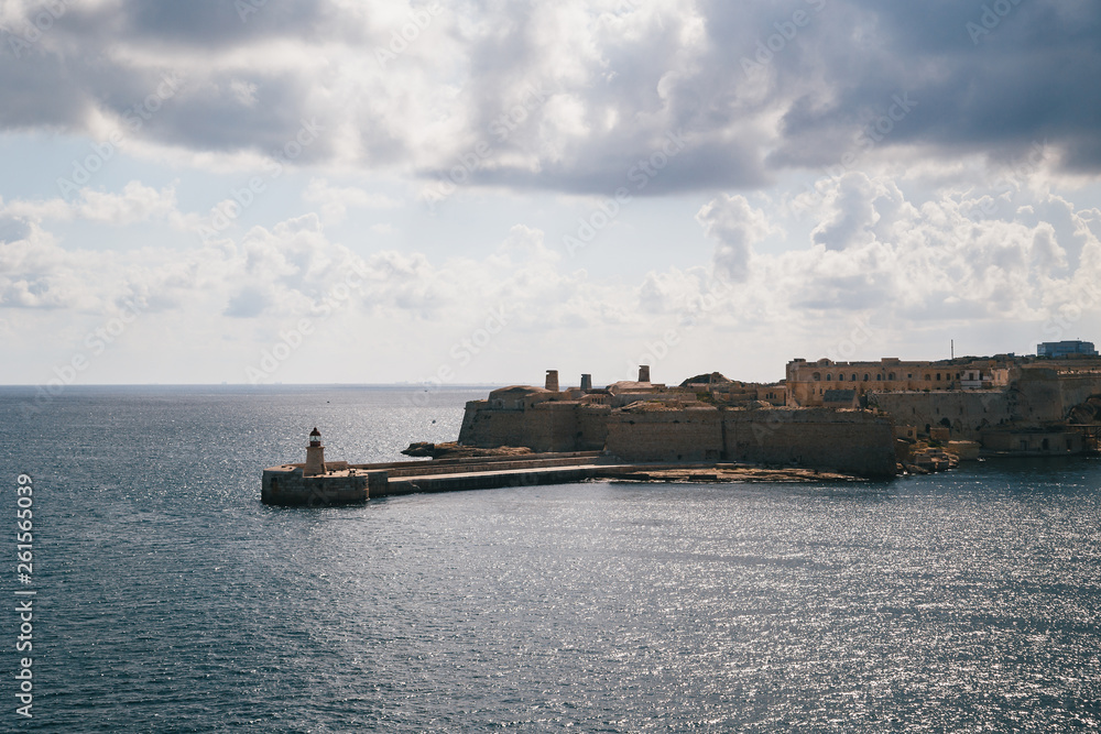 View of the Grand Harbour entrance and old medieval Ricasoli East Breakwater with red lighthouse and Fort Ricasoli seen from Valletta, Malta