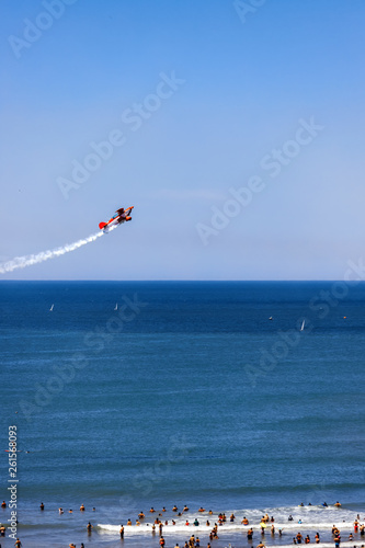Fototapeta Stunt plane overflies sailboats and bathers in the sea near the beach