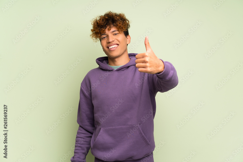 Young african american man over isolated green wall with thumbs up because something good has happened Young african american man over isolated green wall with thumbs up because something good has happened