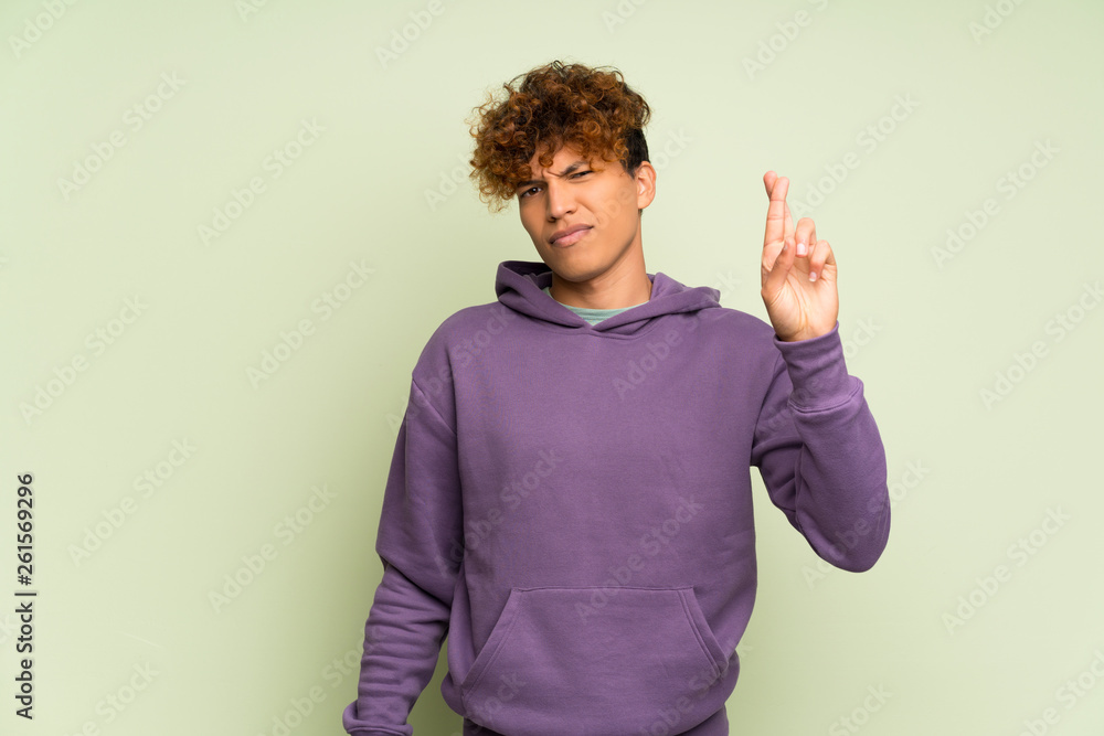 Young african american man over isolated green wall with fingers crossing and wishing the best Young african american man over isolated green wall with fingers crossing and wishing the best