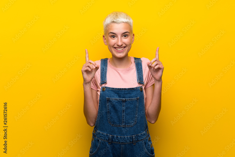 Teenager girl with overalls on yellow background pointing up a great idea Teenager girl with overalls on yellow background pointing up a great idea