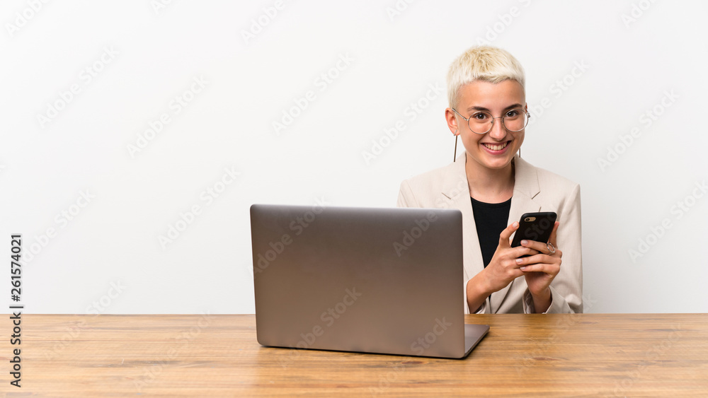 Teenager girl with short hair with a laptop sending a message with the mobile Teenager girl with short hair with a laptop sending a message with the mobile