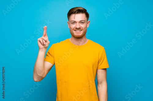 Redhead man over blue wall with fingers crossing and wishing the best © luismolinero