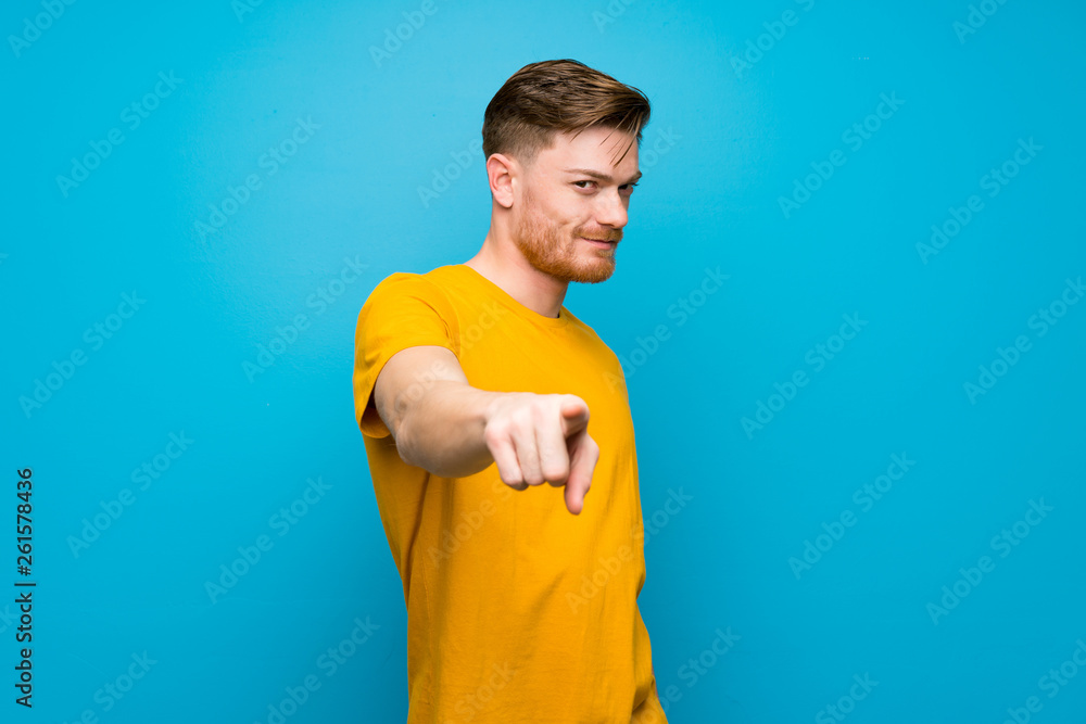 Redhead man over blue wall points finger at you with a confident expression Redhead man over blue wall points finger at you with a confident expression