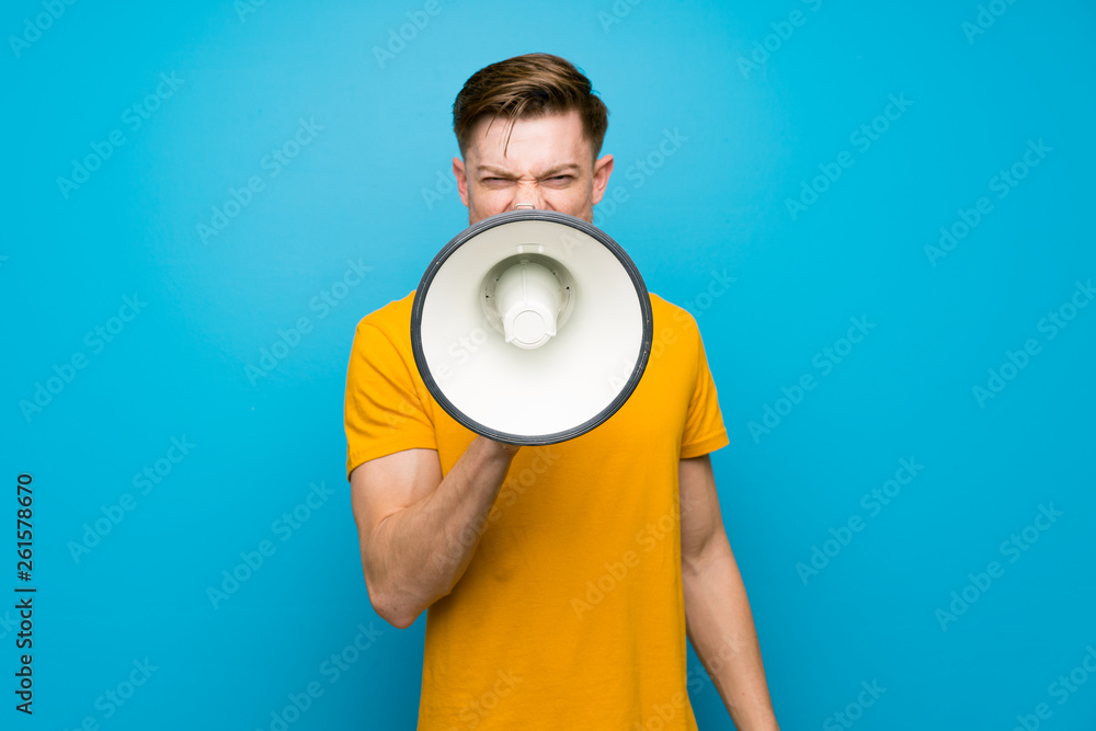 Redhead man over blue wall shouting through a megaphone Redhead man over blue wall shouting through a megaphone