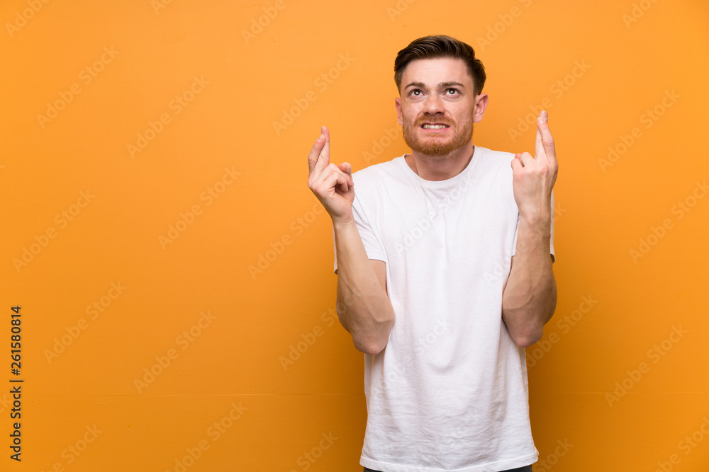 Redhead man over brown wall with fingers crossing and wishing the best Redhead man over brown wall with fingers crossing and wishing the best
