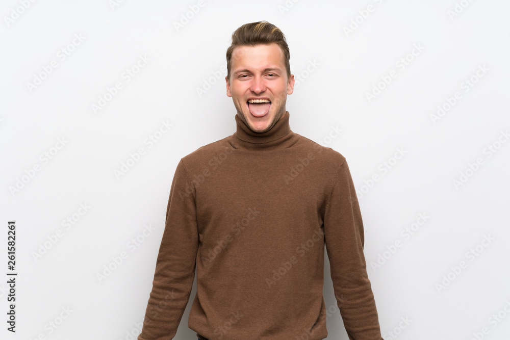 Fototapeta premium Blonde man over isolated white wall showing tongue at the camera having funny look