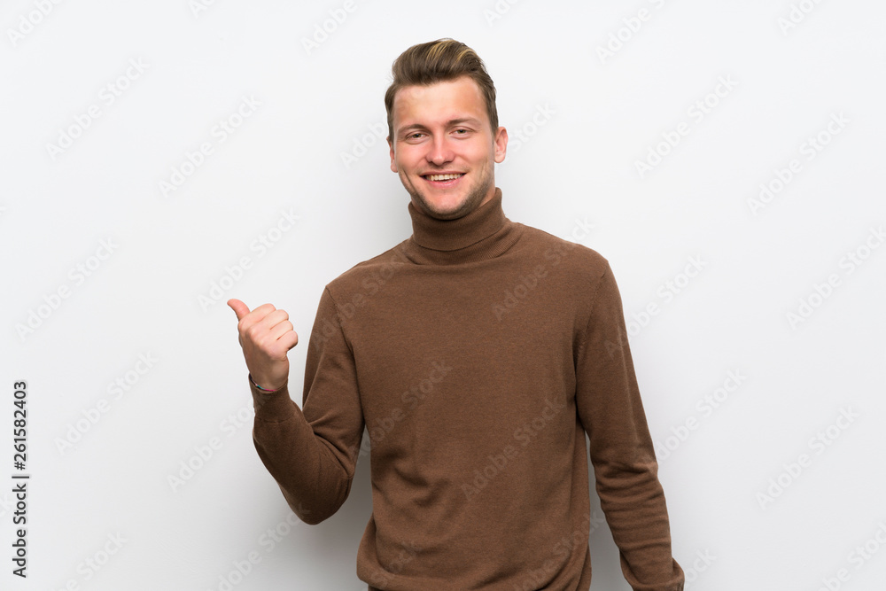 Fototapeta premium Blonde man over isolated white wall pointing to the side to present a product