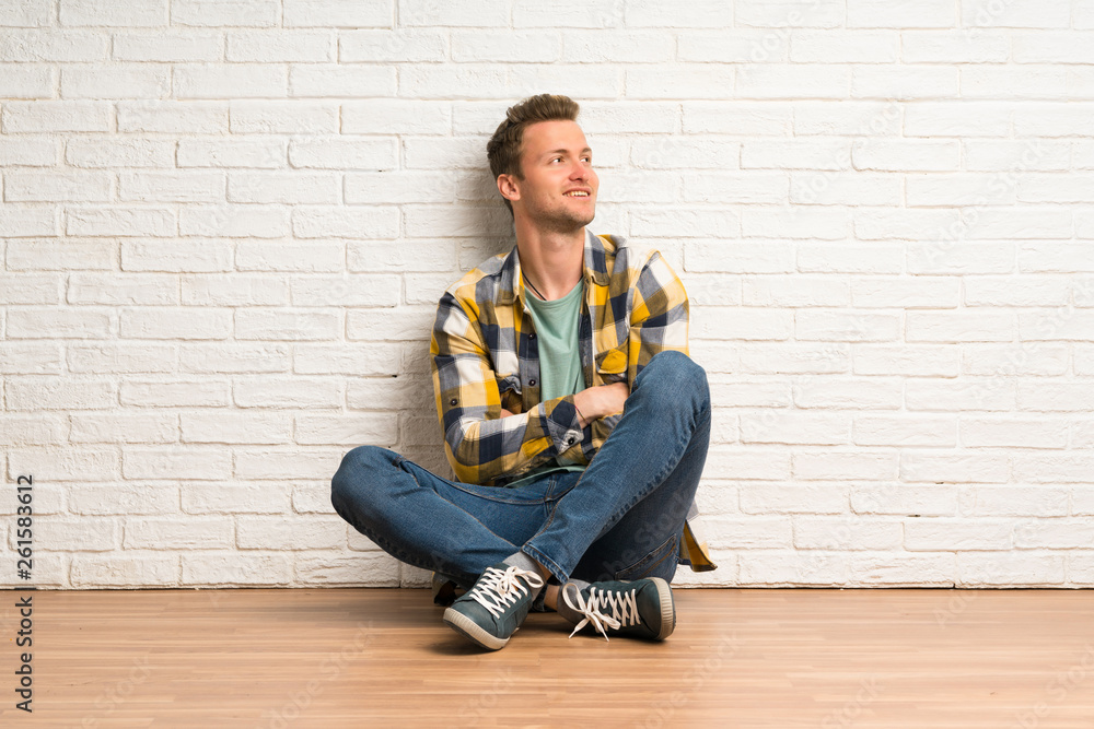 Blonde man sitting on the floor happy and smiling Blonde man sitting on the floor happy and smiling