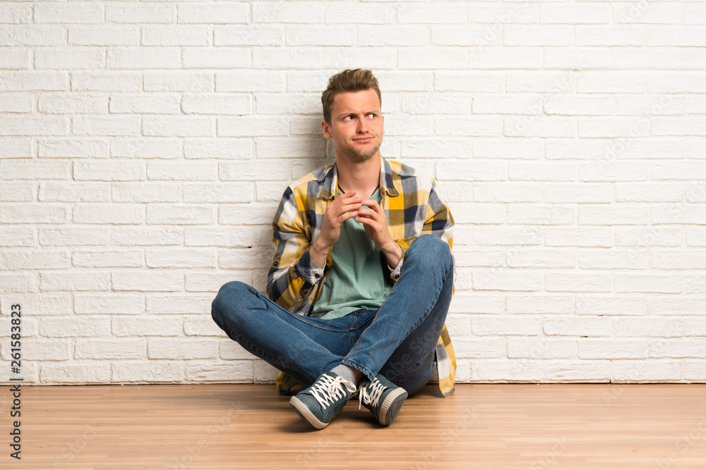 Blonde man sitting on the floor scheming something Blonde man sitting on the floor scheming something