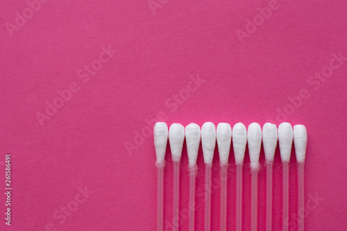 Closeup top view on cotton buds laid in a horizontal line on pink background