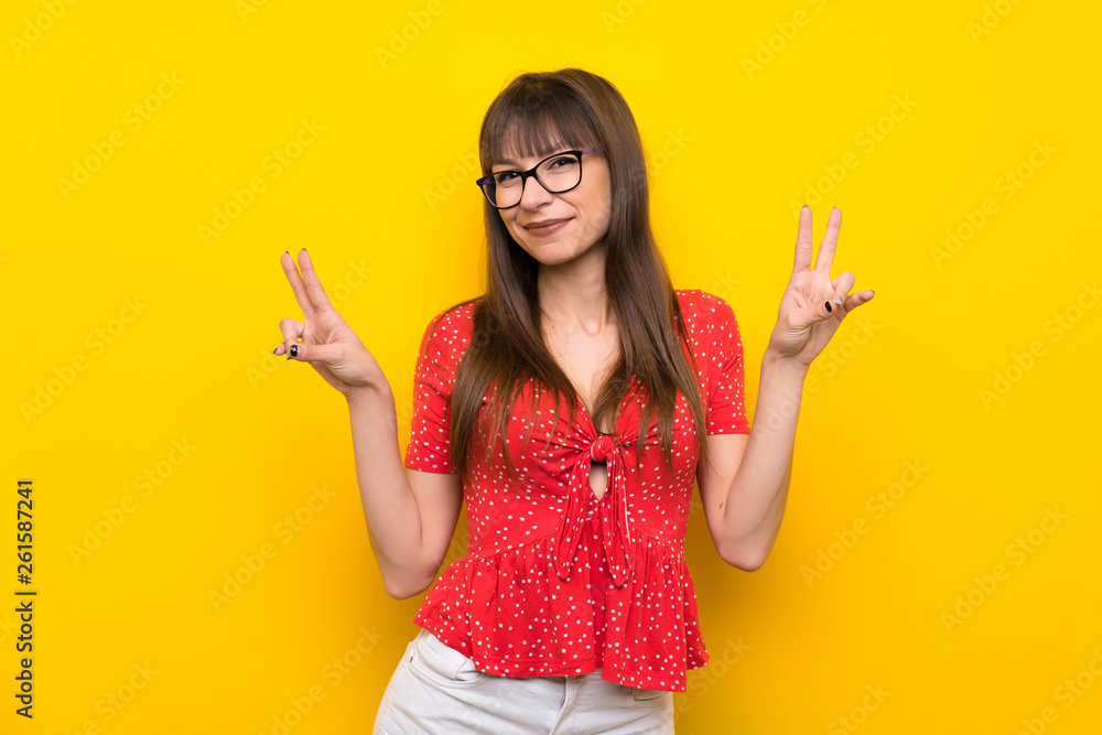 Young woman over yellow wall showing victory sign with both hands Young woman over yellow wall showing victory sign with both hands