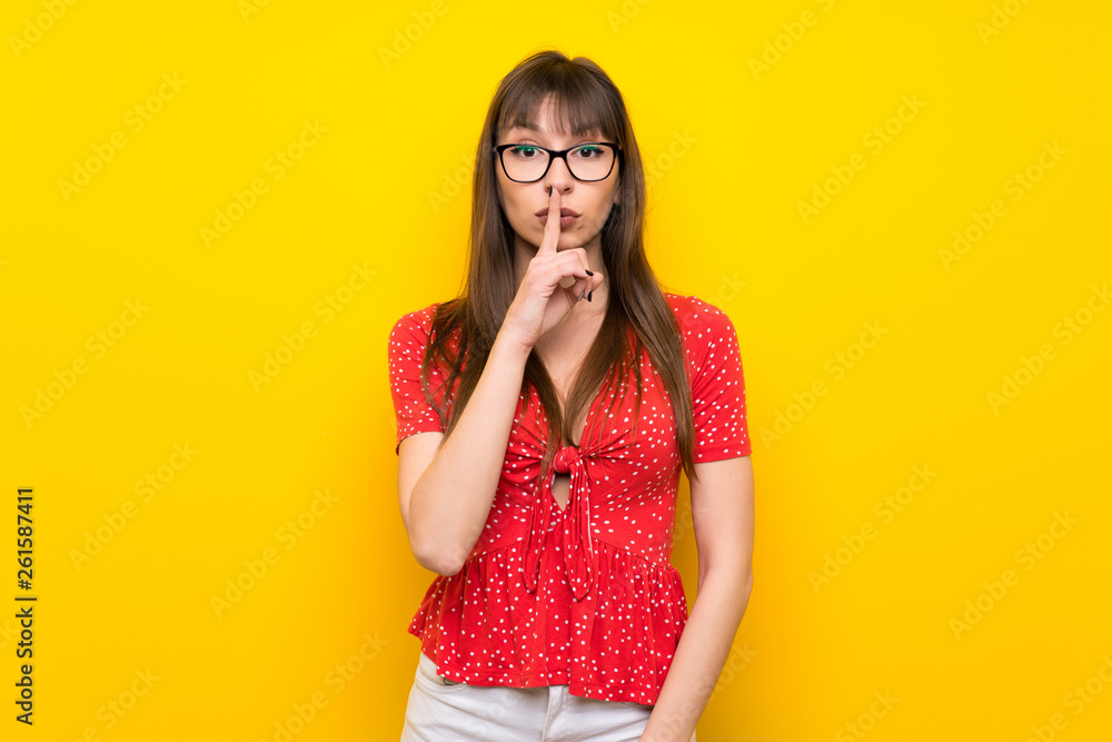 Young woman over yellow wall showing a sign of silence gesture putting finger in mouth Young woman over yellow wall showing a sign of silence gesture putting finger in mouth