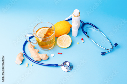 Cold preparations, stethoscope, tea, lemon and ginger root on a blue background. photo