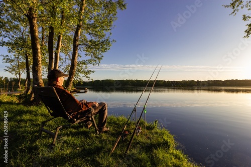 Murais de parede Angler sitting on the shore of the lake during sunrise