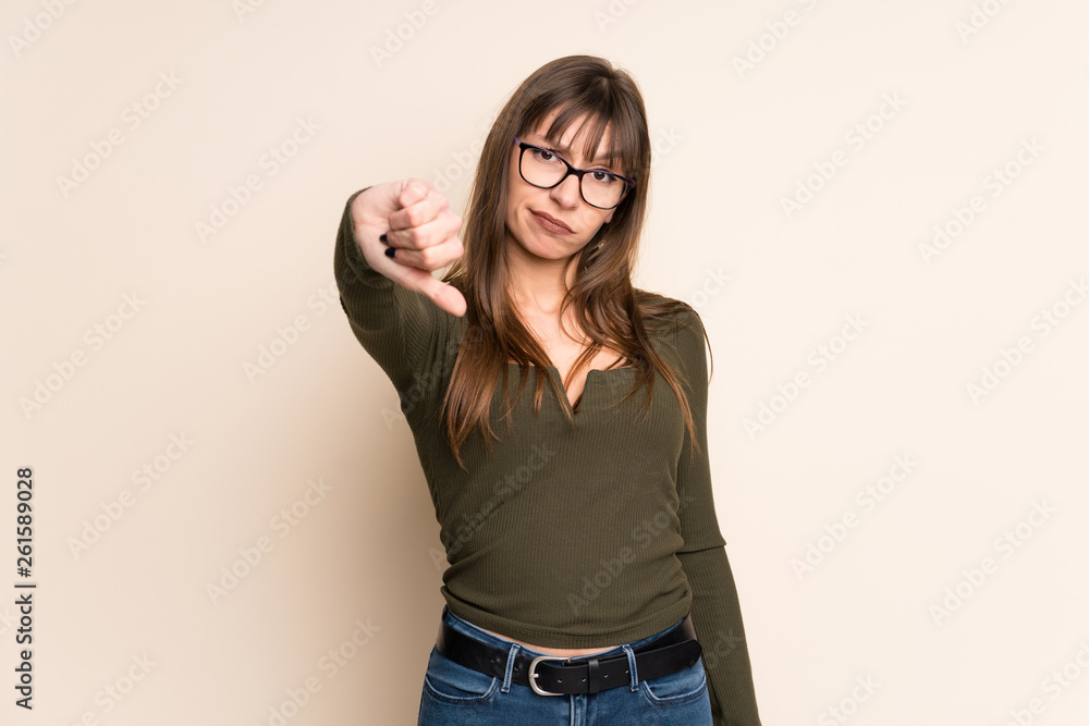 Young woman on ocher background showing thumb down with negative expression Young woman on ocher background showing thumb down with negative expression