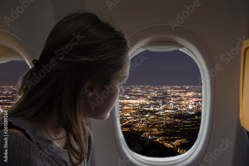 Woman looking out of the plane from the window during a night flight. City lights view