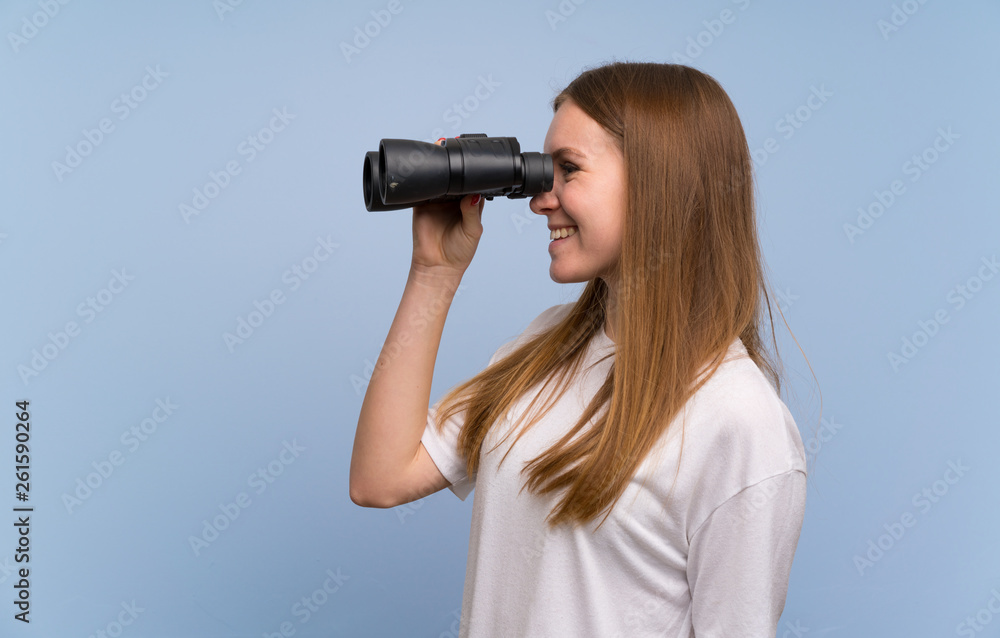 Young woman over blue wall and looking in the distance with binoculars Young woman over blue wall and looking in the distance with binoculars