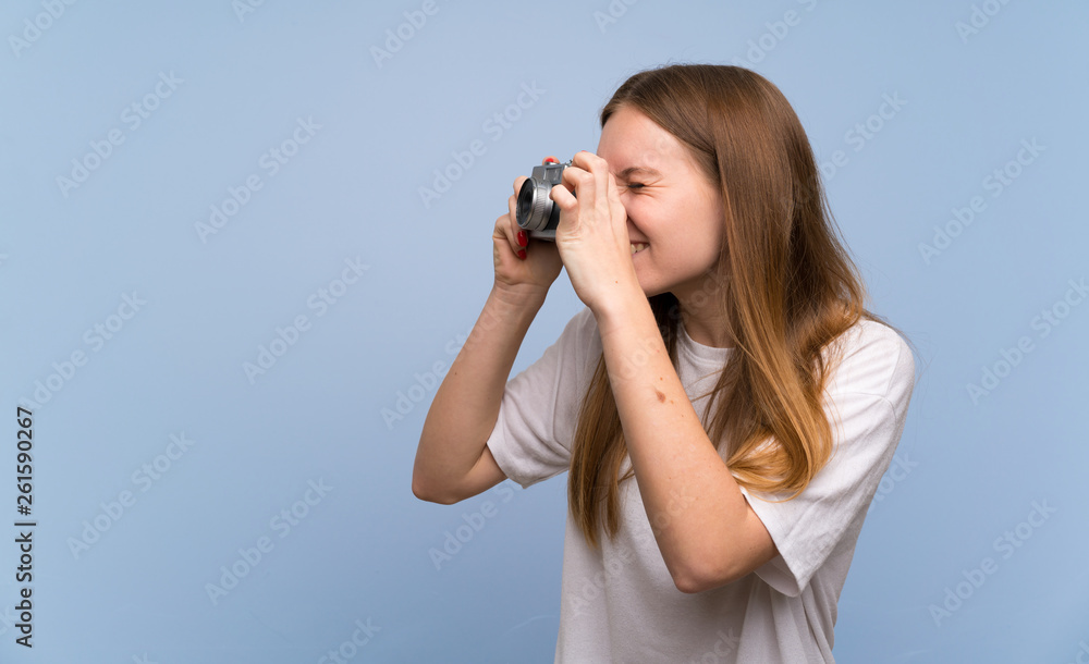 Young woman over blue wall holding a camera