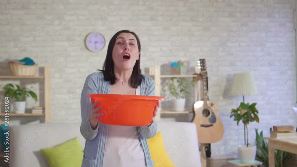 Concerned woman holding a bucket where water flows from the ceiling slow mo Concerned woman holding a bucket where water flows from the ceiling slow mo