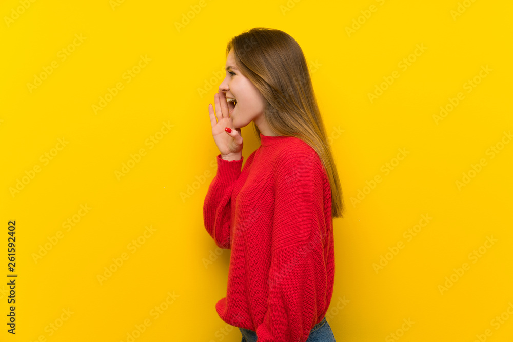 Young woman over yellow wall shouting with mouth wide open to the lateral Young woman over yellow wall shouting with mouth wide open to the lateral